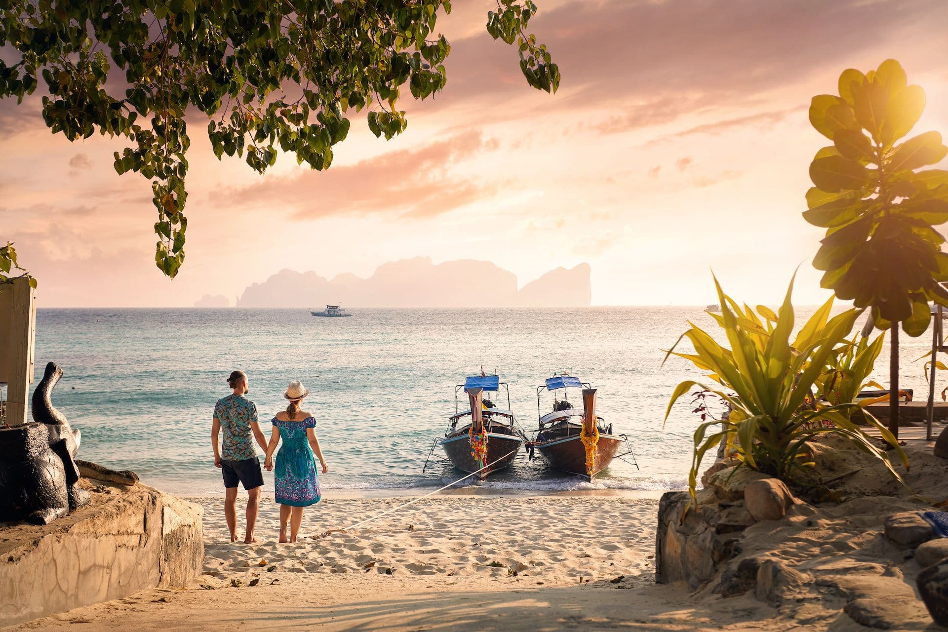 couple on beach thailand two people looking at two boats